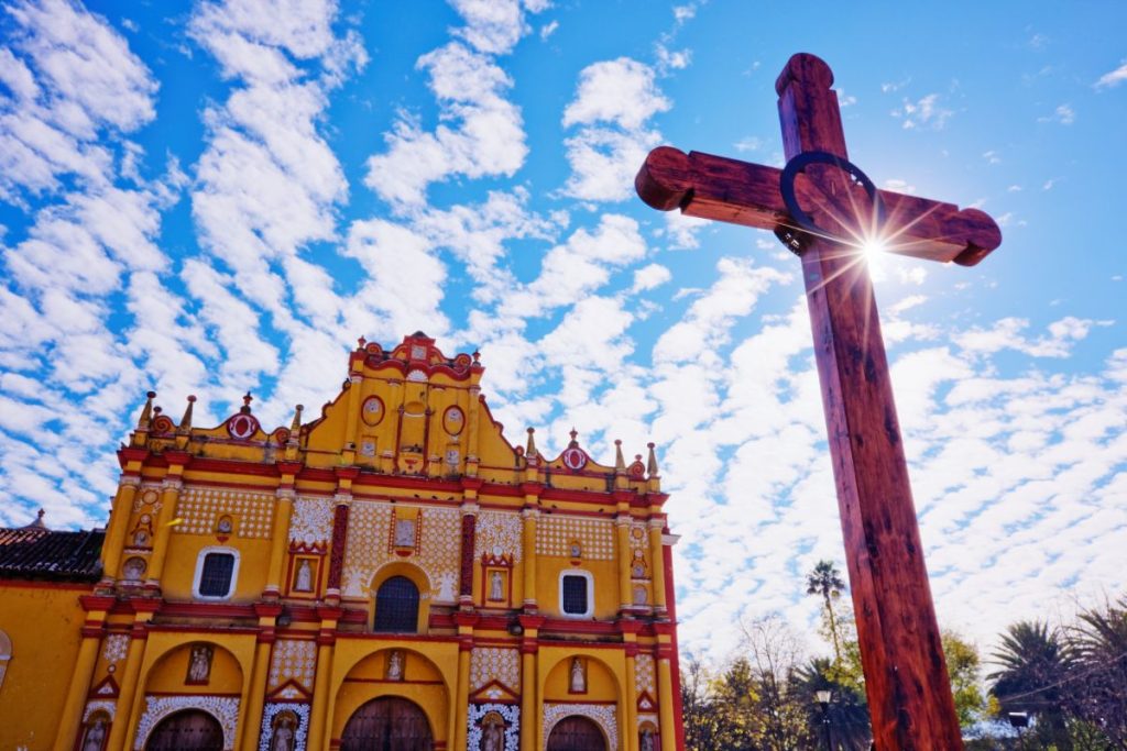 Crucifix in a courtyard in front of an ornate painted church.