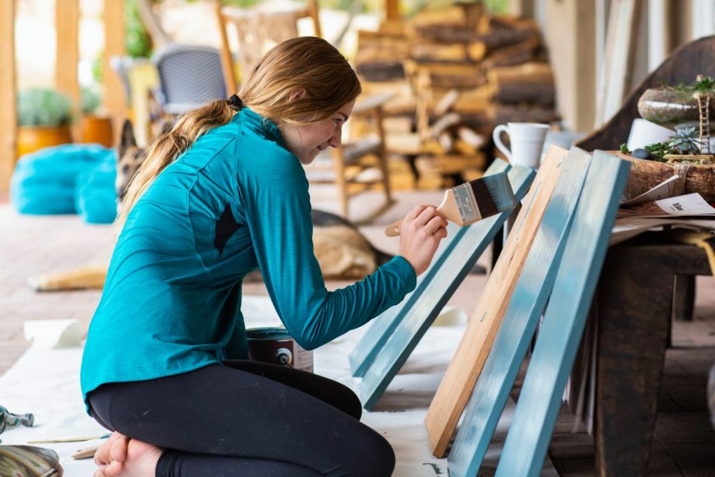 Teenage girl painting wooden shelves blue.