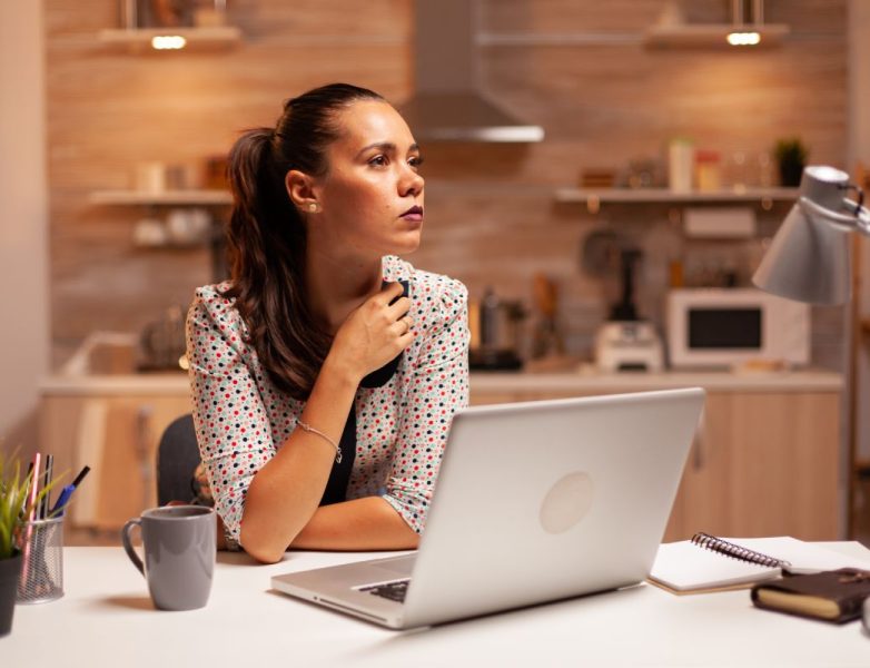 Woman thinking about her career while working on a deadline late at night in home kitchen. Employee using modern technology at midnight doing overtime for job, business, busy, career, network, lifestyle ,wireless.