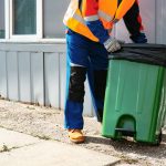 Male janitor in uniform cleans a trash can in the street close up