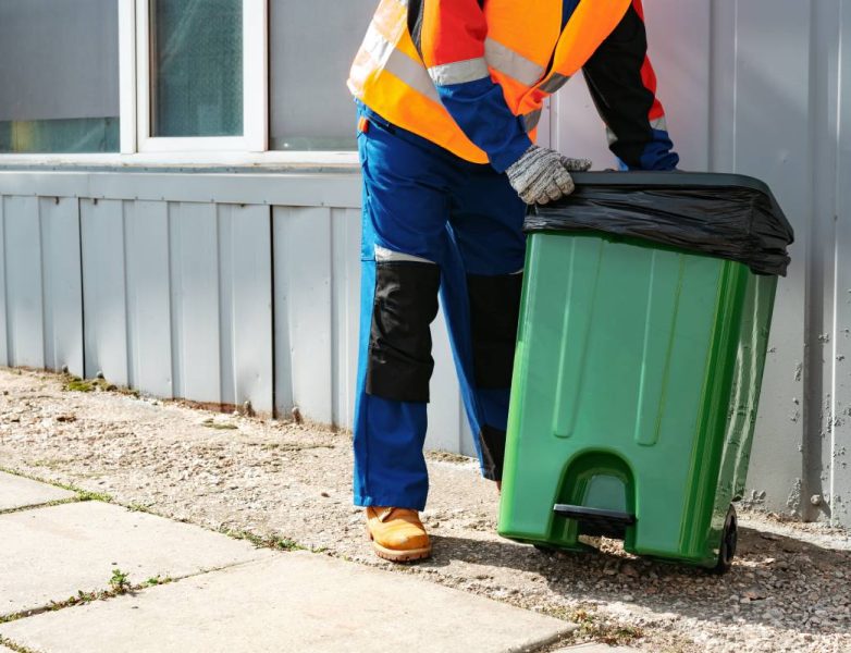 Male janitor in uniform cleans a trash can in the street close up