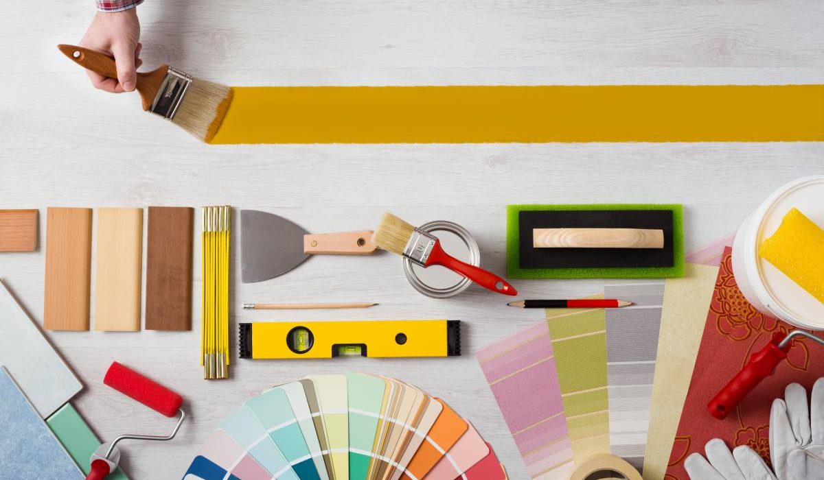 Decorator holding a paint brush and painting a wooden surface, work tools and swatches at bottom, banner with copy space