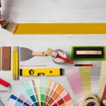 Decorator holding a paint brush and painting a wooden surface, work tools and swatches at bottom, banner with copy space