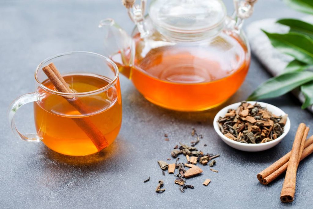 Tea with cinnamon in glass cup and teapot on grey stone background