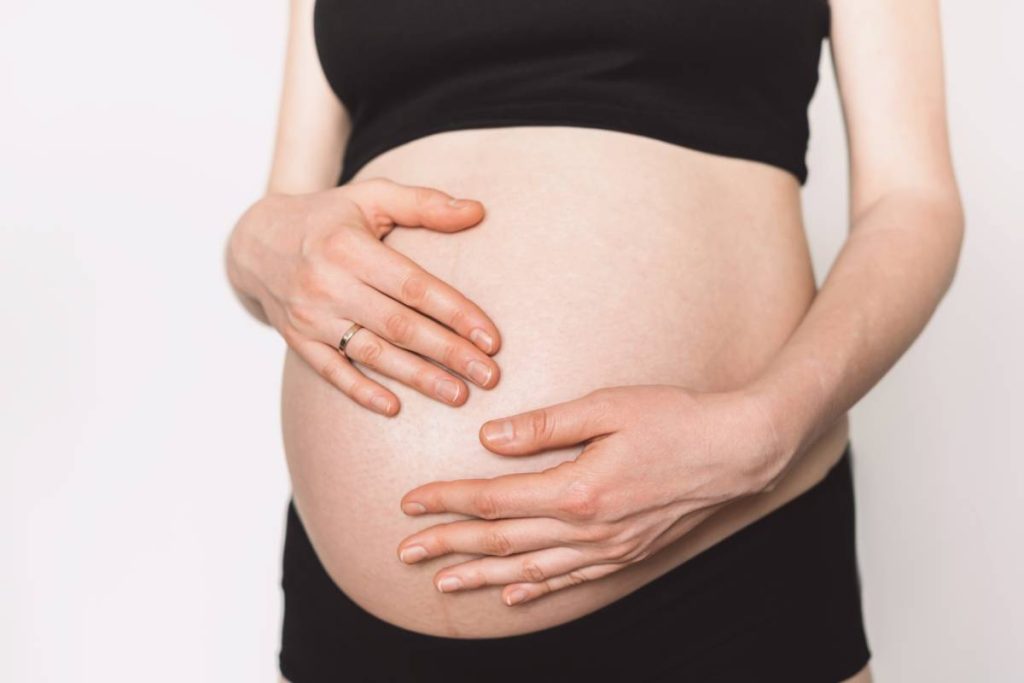 Woman hands touching naked belly. Pregnant woman expecting baby in comfortable top and leggings holding naked pregnant tummy. 40 weeks of pregnancy. Maternity, preparation, baby expectation concept.