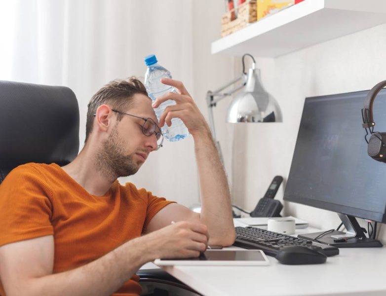 Working at home man suffering from heat and thirst cools down with water bottle at hot summer day. Heat weather without air conditioning