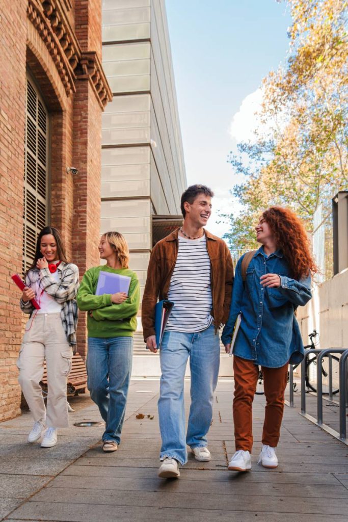 Vertical. Group of smiling high school teenage students walking before starting class, talking together. Diverse classmates carrying notebooks and backpacks going along university. Academy people. High quality photo