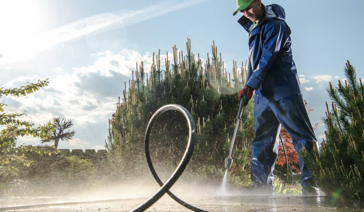 Garden Washing Maintenance. Caucasian Worker in His 30s with Pressure Washer Cleaning Brick Paths.