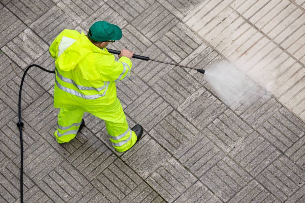 Worker cleaning a pavement sidewalk with high pressure water jet. Maintenance of public areas