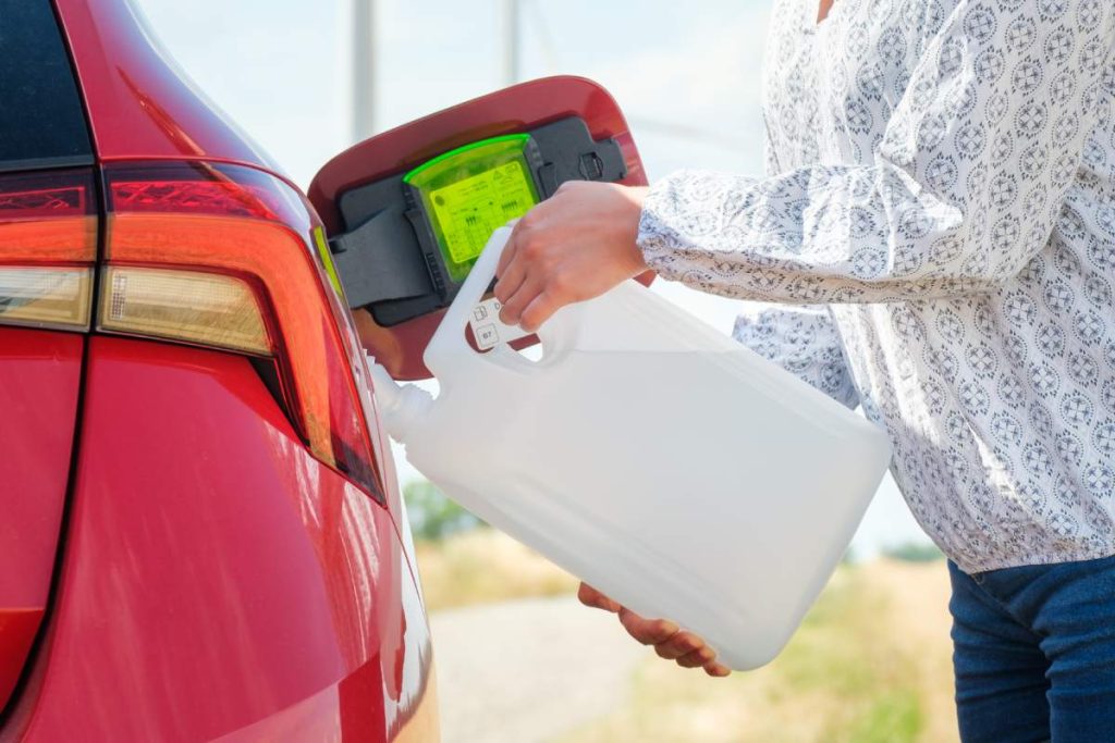 Close up woman refilling the red car with adblue or a diesel engine fluid from canister in the field