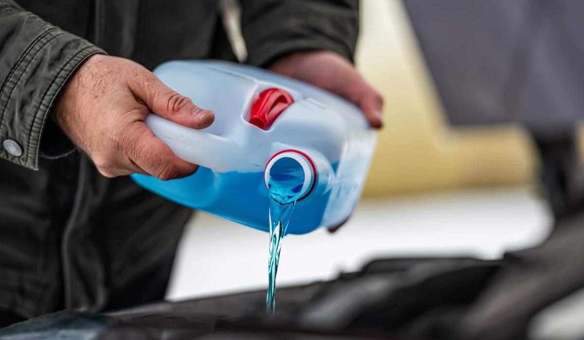 driver refilling the blue non-freezing windshield washer liquid in the tank of the car, closeup