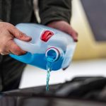 driver refilling the blue non-freezing windshield washer liquid in the tank of the car, closeup