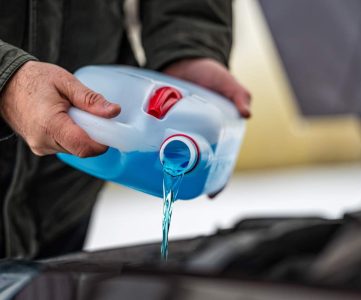 driver refilling the blue non-freezing windshield washer liquid in the tank of the car, closeup