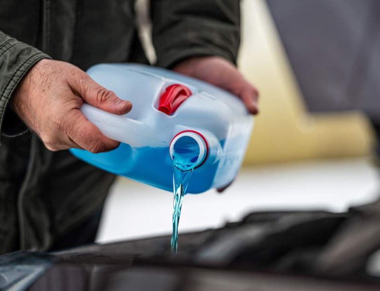 driver refilling the blue non-freezing windshield washer liquid in the tank of the car, closeup