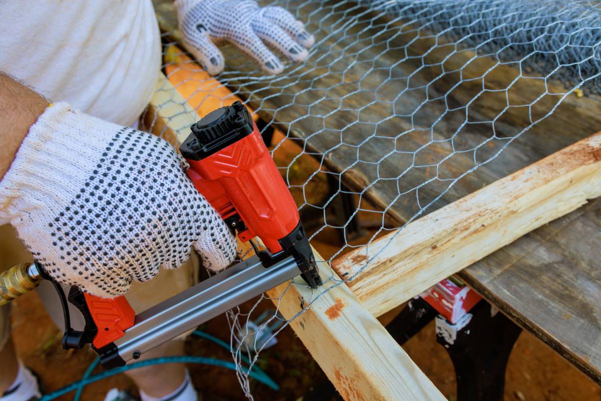 Worker nails metal mesh to wooden frame with help of nail gun