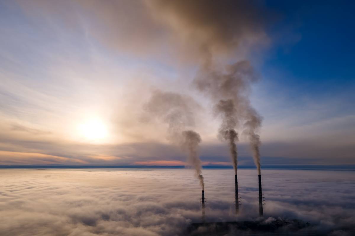 Aerial view of coal power plant high pipes with black smoke moving up polluting atmosphere at sunset.