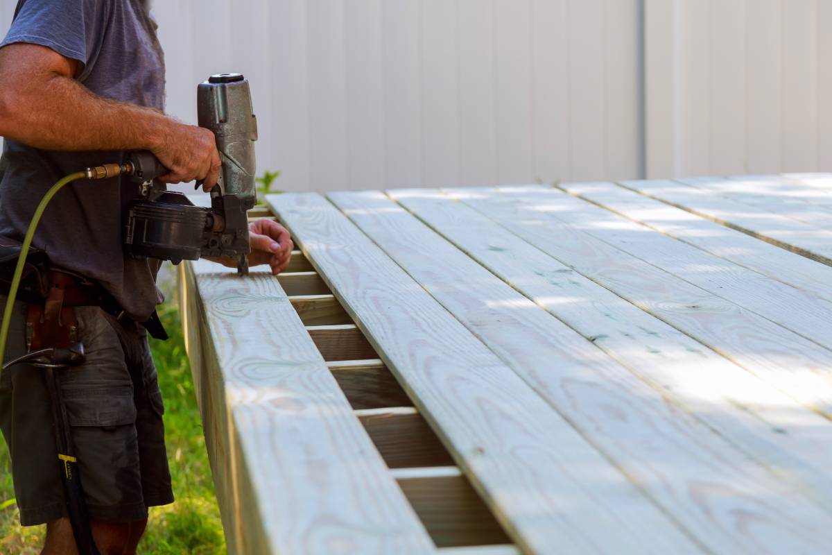 Building a backyard deck with worker putting with nail gun deck boards terrace patio construction.