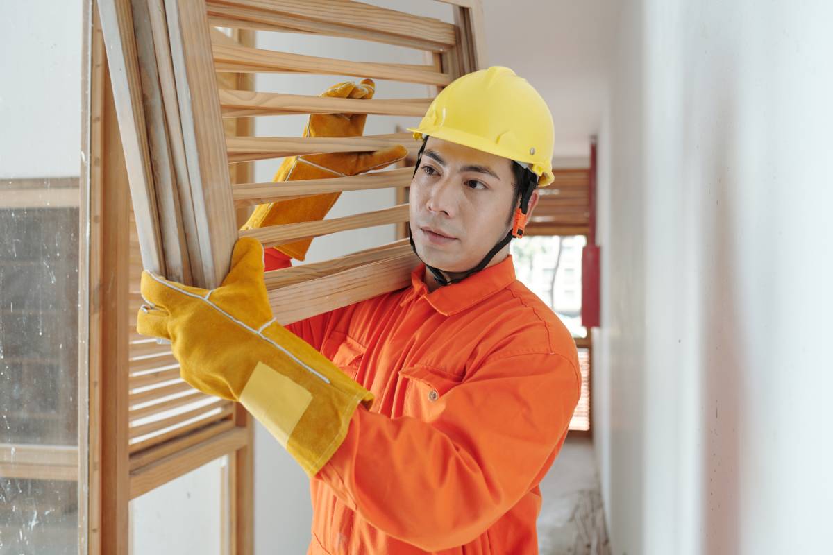 Portrait of serious construction worker carrying heavy wooden grates when walking along corridor in house