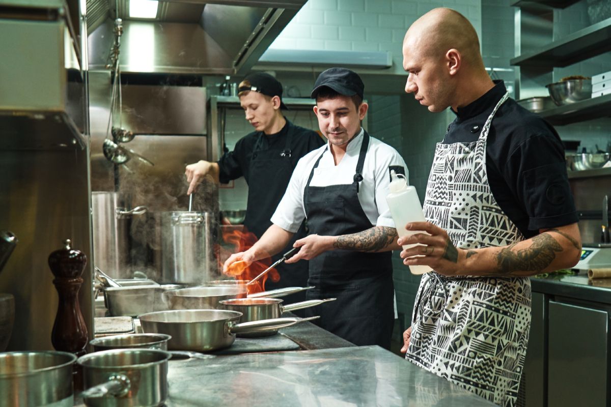 Dangerous work. Profesional chef teaching his two young trainees how how to flambe food safely. Cooking techniques. Culinary school