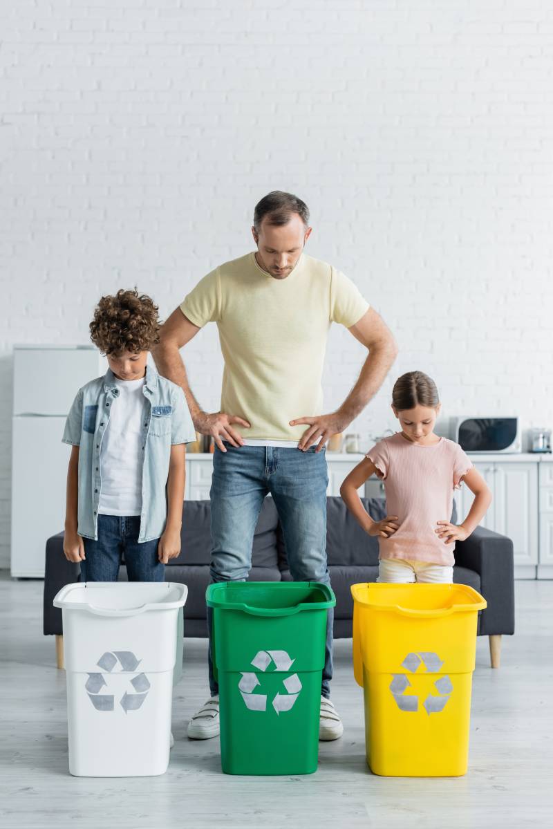 Father and kids looking at trash bins with recycle sign in kitchen