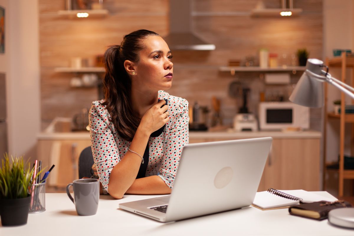Woman thinking about her career while working on a deadline late at night in home kitchen. Employee using modern technology at midnight doing overtime for job, business, busy, career, network, lifestyle ,wireless.
