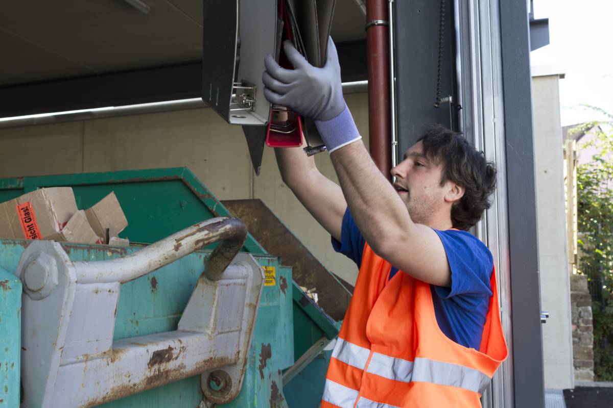 Worker at a waste container throwing away folders