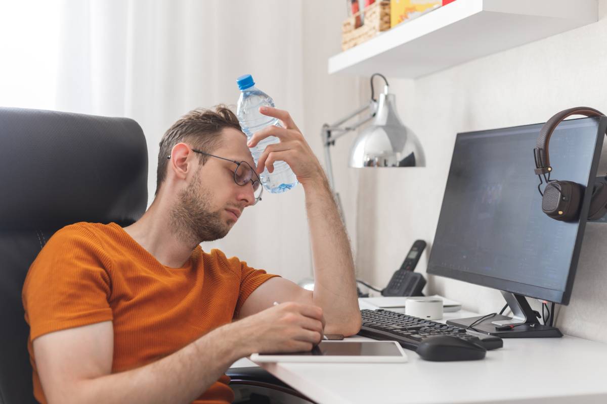 Working at home man suffering from heat and thirst cools down with water bottle at hot summer day. Heat weather without air conditioning